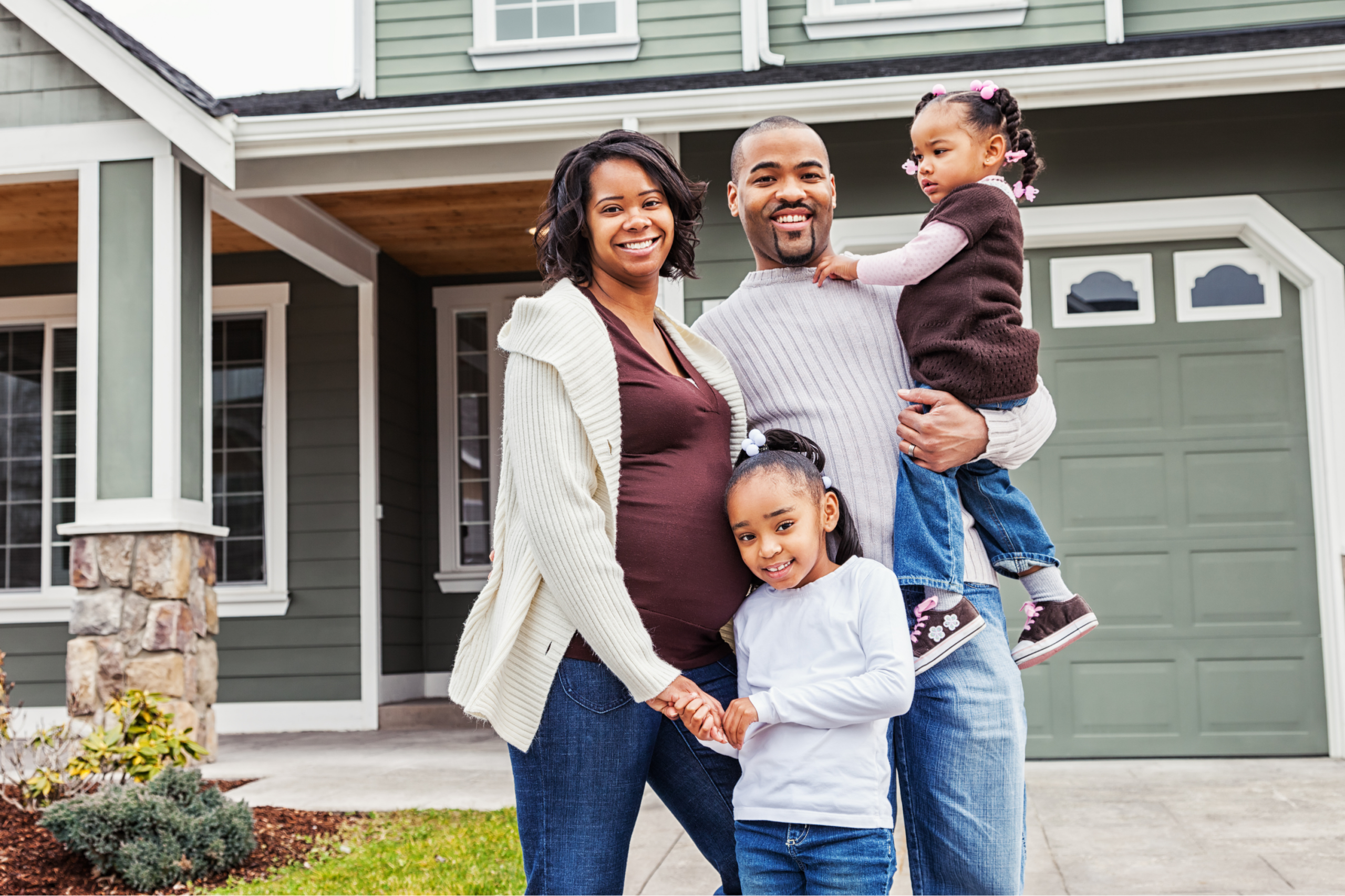 Happy family of four standing in front of their house.
