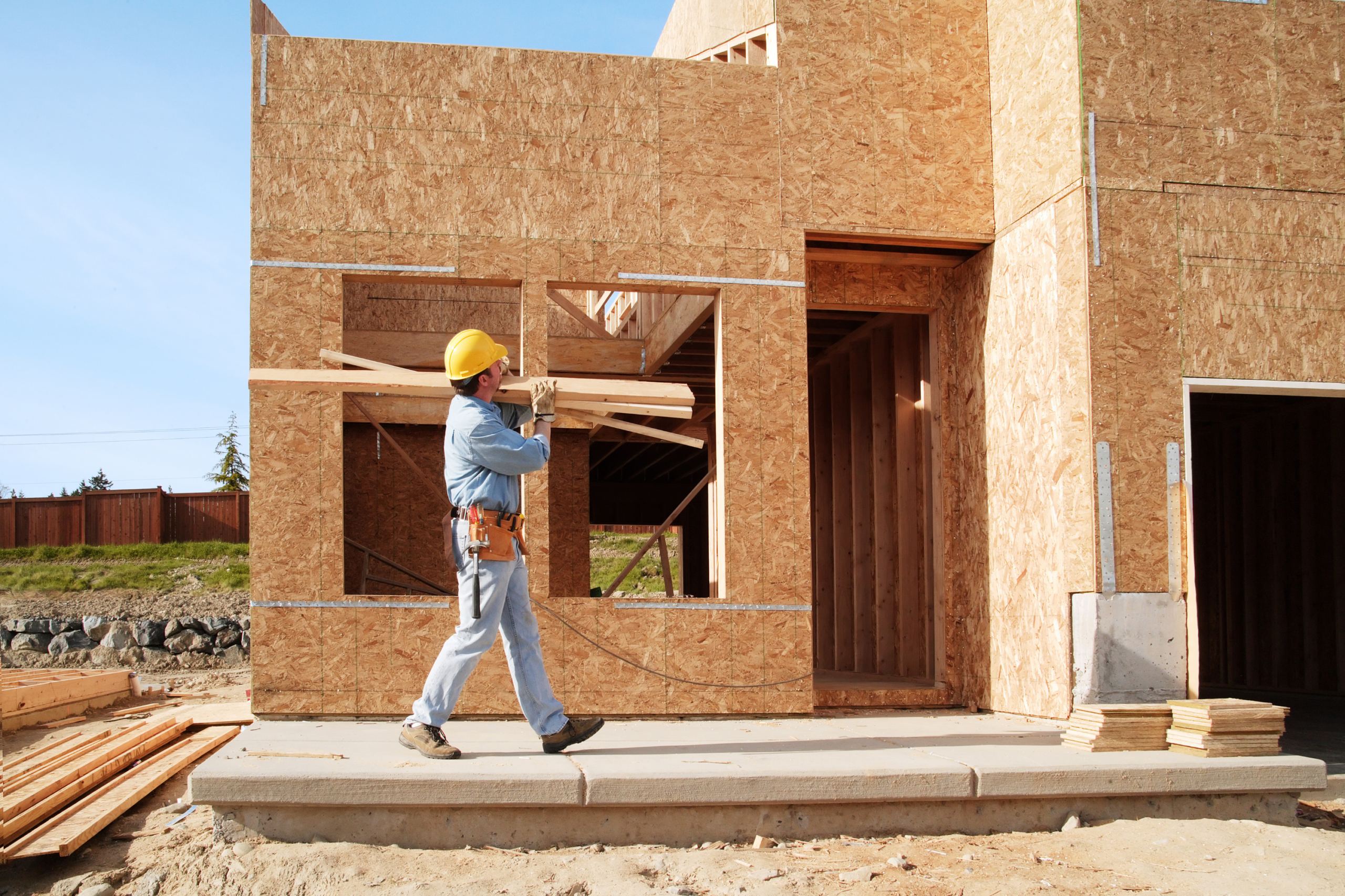 Worker at a new home construction job site walking with lumber on his shoulder.