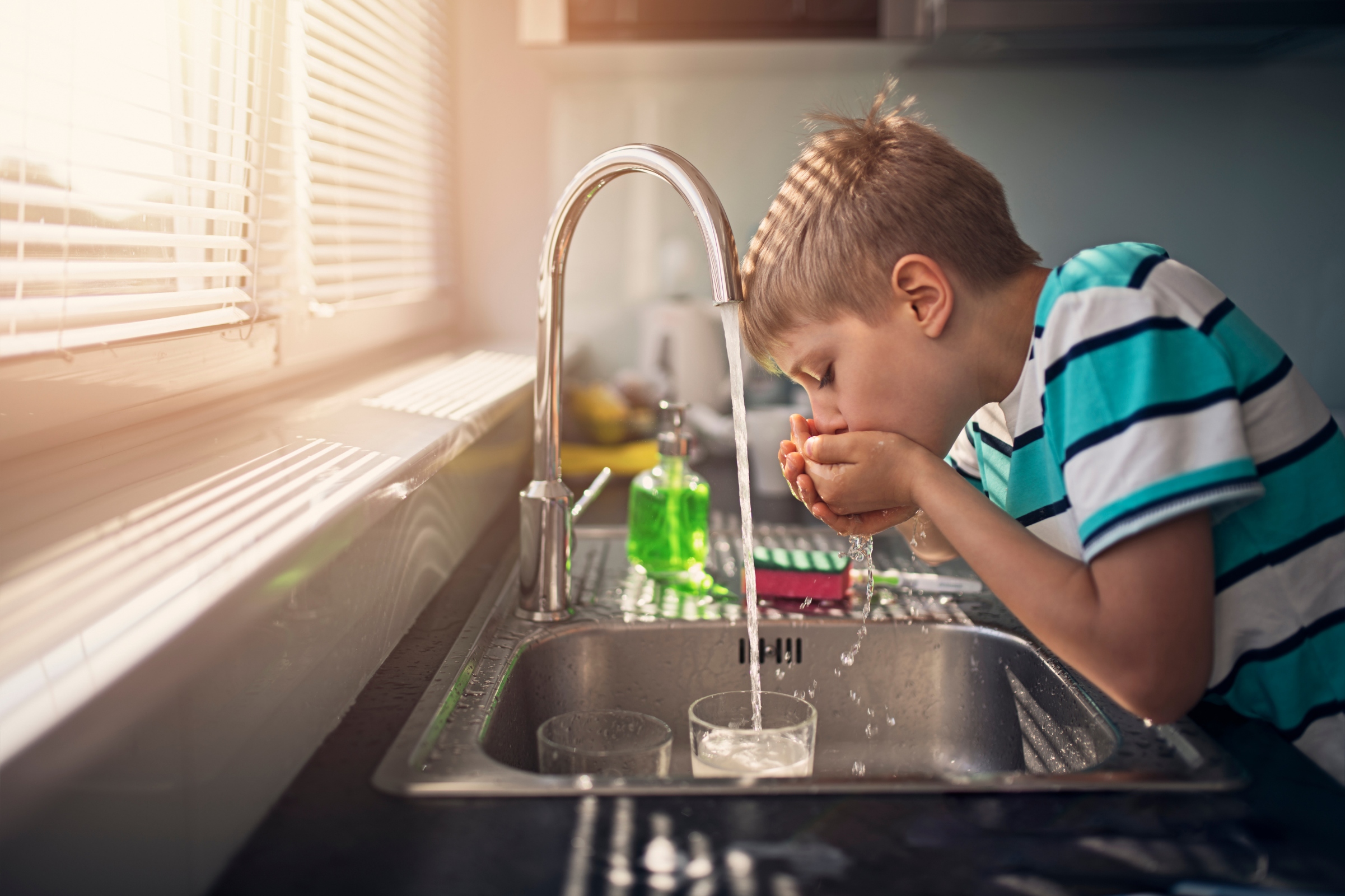 Child using his hands to drink tap water from the kitchen sink.