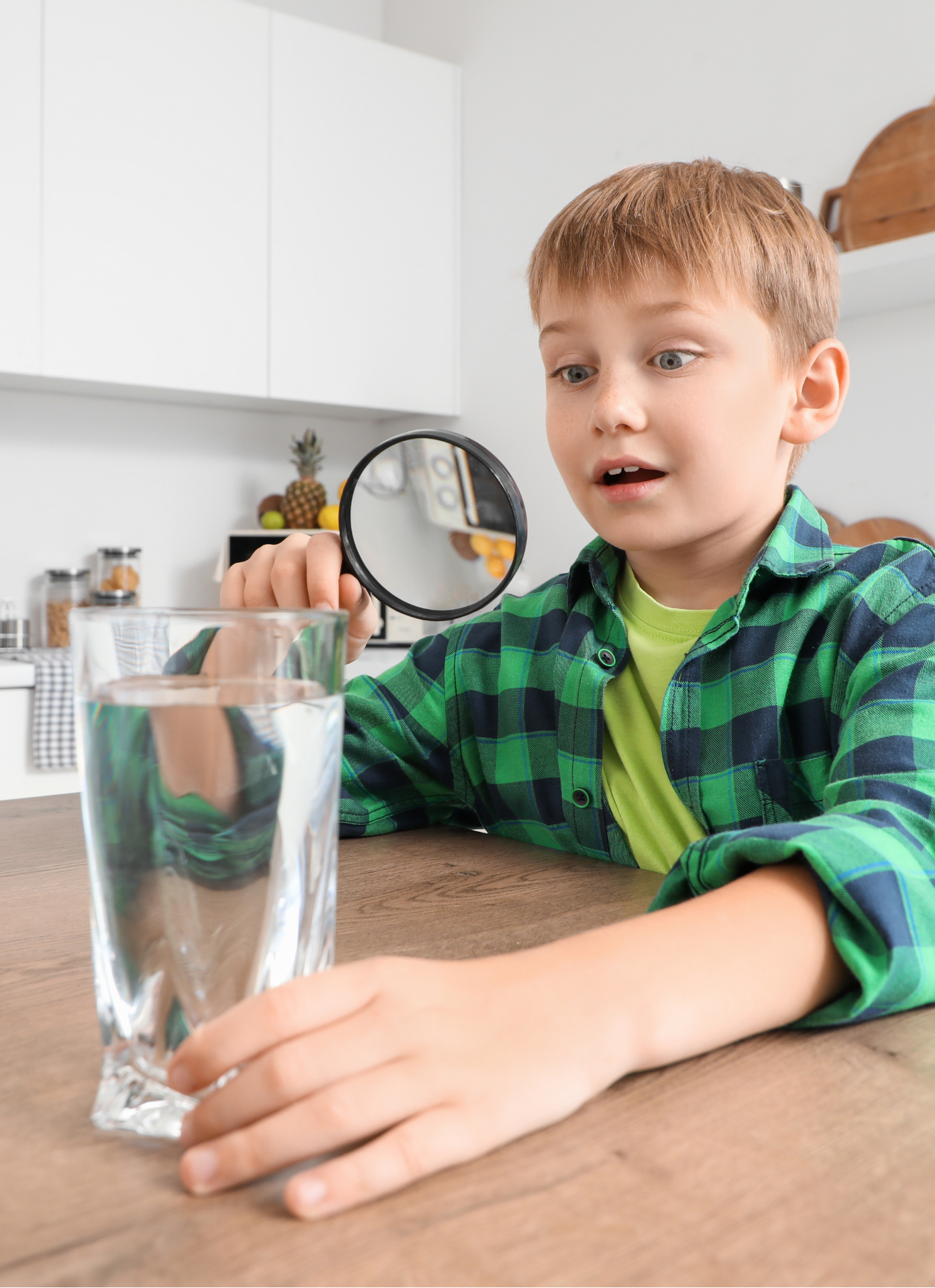 Child holding a magnifying glass to a glass of water.